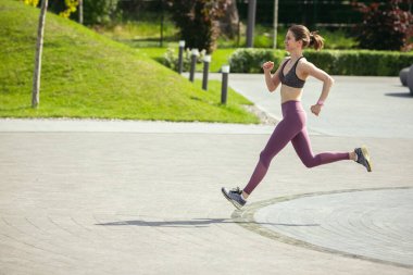 Genç bayan koşucu, atlet bahar güneşinde şehir caddesinde koşuyor. Güzel beyaz kadın eğitimi, müzik dinlemek. Spor anlayışı, sağlıklı yaşam tarzı, hareket, aktivite.