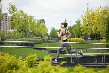 Genç bayan koşucu, atlet bahar güneşinde şehir caddesinde koşuyor. Güzel beyaz kadın eğitimi, müzik dinlemek. Spor anlayışı, sağlıklı yaşam tarzı, hareket, aktivite.