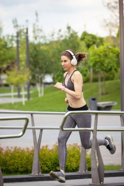 Genç bayan koşucu, atlet bahar güneşinde şehir caddesinde koşuyor. Güzel beyaz kadın eğitimi, müzik dinlemek. Spor anlayışı, sağlıklı yaşam tarzı, hareket, aktivite.