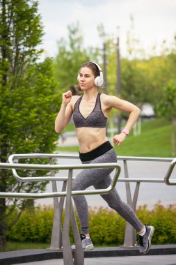 Genç bayan koşucu, atlet bahar güneşinde şehir caddesinde koşuyor. Güzel beyaz kadın eğitimi, müzik dinlemek. Spor anlayışı, sağlıklı yaşam tarzı, hareket, aktivite.