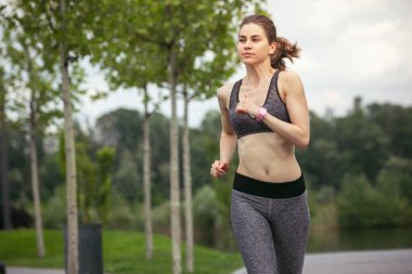 Genç bayan koşucu, atlet bahar güneşinde şehir caddesinde koşuyor. Güzel beyaz kadın eğitimi, müzik dinlemek. Spor anlayışı, sağlıklı yaşam tarzı, hareket, aktivite.