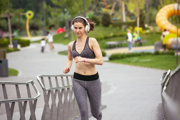 Junge Läuferin, Athletin joggt in der Frühlingssonne auf der Stadtstraße. Schöne kaukasische Frau, die trainiert und Musik hört. Konzept von Sport, gesunder Lebensweise, Bewegung, Aktivität. — Stockfoto