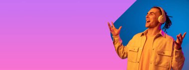 Genç yakışıklı adam, mavi mor arka planda, neon ışıkta izole edilmiş müzik dinliyor. Güzellik kavramı, moda, reklam. El ilanı