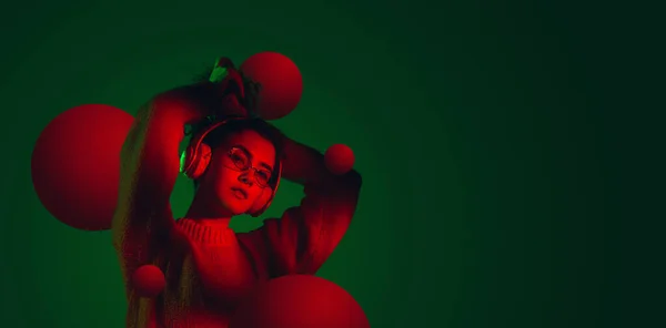 Giovane bella ragazza caucasica ascoltare musica isolata su sfondo verde scuro in luce al neon. Concetto di bellezza, moda, annuncio. Volantino — Foto Stock