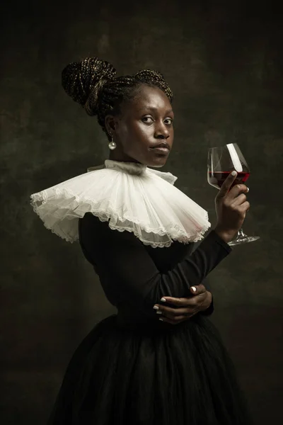 Portrait of medieval African young woman in black vintage dress with big white collar posing isolated on dark green background. Cheers