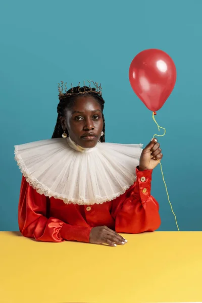 Retrato de jovem mulher africana em vestido vintage vermelho brilhante com grande colar branco posando isolado no fundo azul. Conceito de comparação de eras, moda, humor, anúncio. — Fotografia de Stock