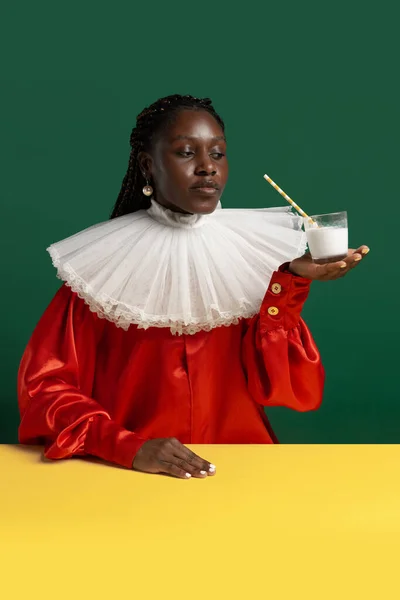 Eine junge Afrikanerin in leuchtend rotem Vintage-Kleid mit großem weißen Kragen posiert isoliert auf grünem Hintergrund. Konzept des Zeitvergleichs, Mode, Humor, Werbung. — Stockfoto