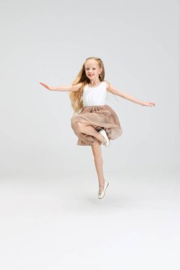 Modern modaya uygun giyinmiş, beyaz stüdyo arka planında yalnız poz veren güzel bir kız. Mutlu çocukluk kavramı.