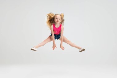 Beyaz stüdyo arka planında izole edilmiş, gündelik kıyafetlerle atlayan güzel bir kız. Mutlu çocukluk kavramı.