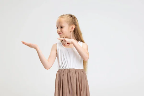 Portrait de demi-longueur de mignonne petite fille en robe élégante moderne posant isolée sur fond de studio blanc. Concept d'enfance heureuse. — Photo