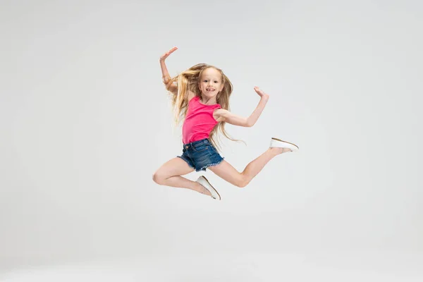 Belle petite fille en vêtements décontractés sautant isolé sur fond de studio blanc. Concept d'enfance heureuse. — Photo