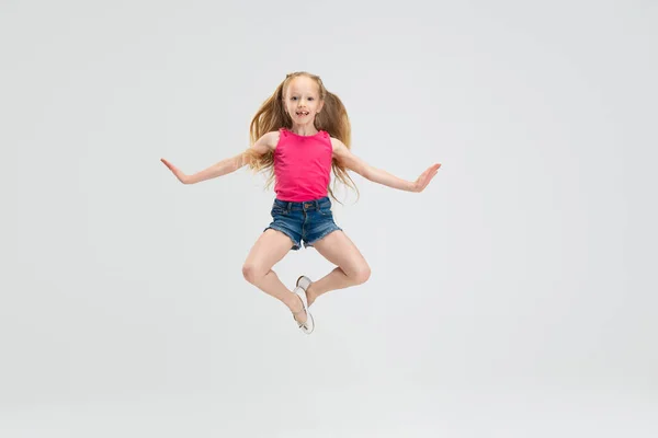 Belle petite fille en vêtements décontractés sautant isolé sur fond de studio blanc. Concept d'enfance heureuse. — Photo