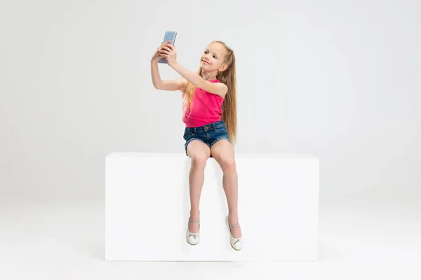 Una hermosa niña con ropa casual sentada en una caja aislada sobre fondo blanco del estudio. Concepto de infancia feliz. —  Fotos de Stock