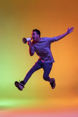 Bir Latin genç adam megafonlu, hoparlör hoparlörlü, yüksek yalıtılmış yeşil arka planda neon ışıklarıyla zıplıyor..