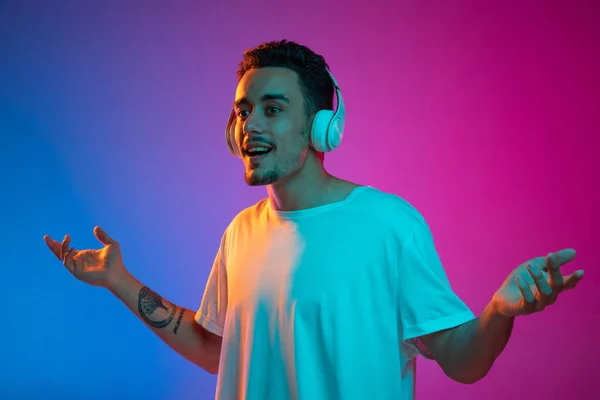 Retrato de un joven latino en audífonos blancos escuchando música aislada sobre fondo rosa púrpura degradado en luz de neón. — Foto de Stock