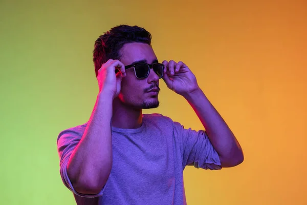 Porträt von Latina junger Mann in Sonnenbrille posiert isoliert auf Gradienten gelb-grünen Hintergrund in Neonlicht. — Stockfoto