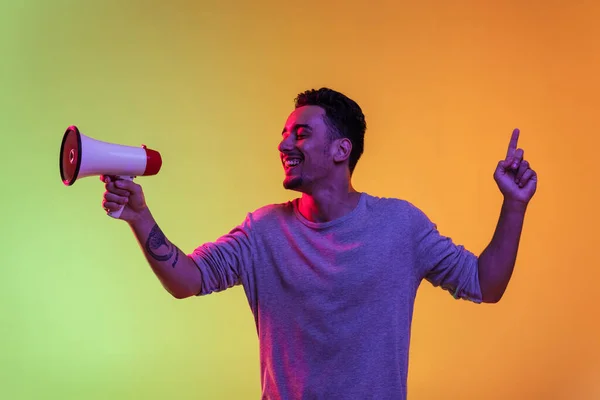 One Latina young man with megaphone, loudspeaker standing hands up isolated on gradient yellow green background in neon light. — Stock Photo, Image