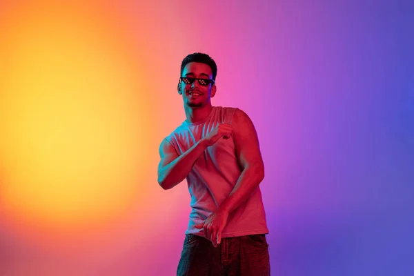 Retrato do jovem latino, dançarino apresentando-se isolado em gradiente amarelo fundo roxo em luz de néon. Conceito de emoções, expressão facial — Fotografia de Stock