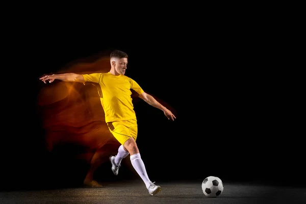 Jovens caucasianos do futebol masculino ou jogador de futebol treinando em luz mista isolados em fundo escuro. Conceito de estilo de vida saudável, esporte profissional, ativo, movimento.. — Fotografia de Stock