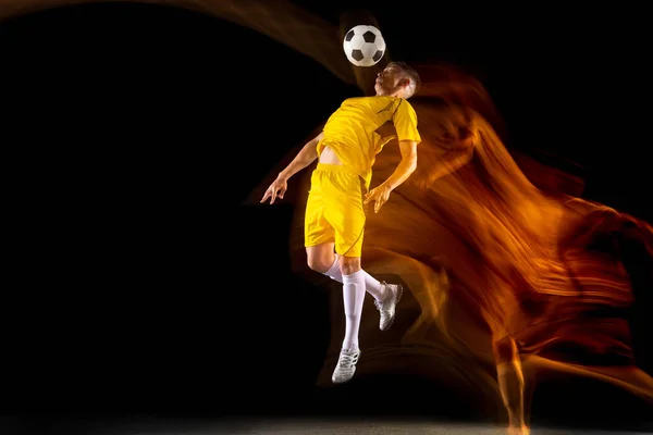 Een Kaukasische mannelijke voetbal of voetbal speler training met bal in gemengd licht geïsoleerd op donkere achtergrond. Begrip professionele sport, actief, beweging. — Stockfoto