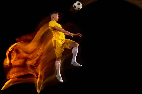 Młody biały mężczyzna piłki nożnej lub piłkarz trening w mieszanym świetle izolowane na ciemnym tle. Pojęcie zdrowego trybu życia, sportu zawodowego, aktywnego, ruchu.. — Zdjęcie stockowe