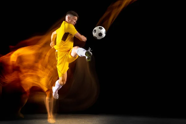 Een Kaukasische mannelijke voetbal of voetbal speler training met bal in gemengd licht geïsoleerd op donkere achtergrond. Begrip professionele sport, actief, beweging. — Stockfoto