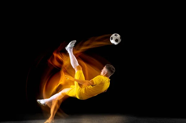 Een Kaukasische mannelijke voetbal of voetbal speler training met bal in gemengd licht geïsoleerd op donkere achtergrond. Begrip professionele sport, actief, beweging.. — Stockfoto