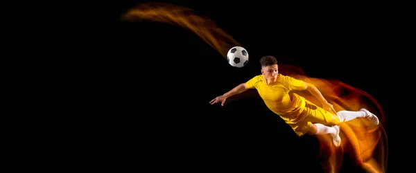 O Flyer. Um jogador caucasiano de futebol masculino ou futebol treinando com bola em luz mista isolado em fundo escuro. Conceito de esporte profissional, ativo, movimento.. — Fotografia de Stock