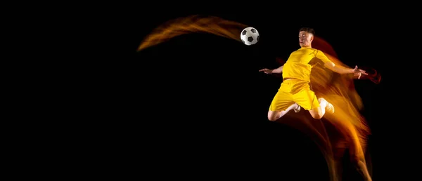 Ulotka. Jeden biały mężczyzna piłki nożnej lub piłkarz trening z piłką w mieszanym świetle izolowane na ciemnym tle. Pojęcie sportu profesjonalnego, aktywnego, ruchu.. — Zdjęcie stockowe