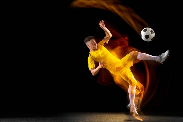 Jeden kavkazský mužský fotbal nebo fotbalista trénuje s míčem ve smíšeném světle izolovaném na tmavém pozadí. Pojetí profesionálního sportu, aktivní, pohyblivý. — Stock fotografie