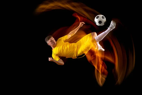 Salah satu sepak bola laki-laki kaukasia atau pemain sepak bola berlatih dengan bola dalam cahaya campuran terisolasi di latar belakang gelap. Konsep olahraga profesional, aktif, gerak.. — Stok Foto