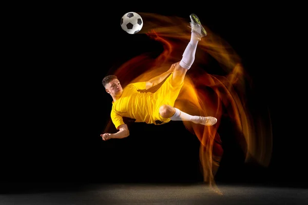 Jeden biały mężczyzna piłki nożnej lub piłkarz trening z piłką w mieszanym świetle izolowane na ciemnym tle. Pojęcie sportu profesjonalnego, aktywnego, ruchu. — Zdjęcie stockowe