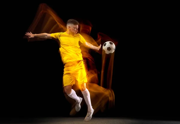 Ένας καυκάσιος αρσενικό ποδόσφαιρο ή ποδοσφαιριστής κατάρτισης με μπάλα σε μικτή φως απομονώνονται σε σκούρο φόντο. Έννοια του επαγγελματικού αθλητισμού, ενεργό, κίνηση. — Φωτογραφία Αρχείου