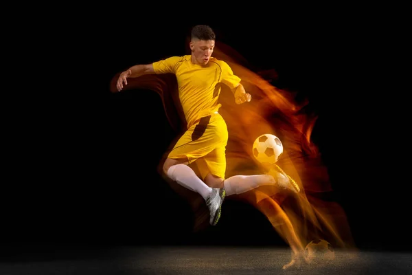 Jeden biały mężczyzna piłki nożnej lub piłkarz trening z piłką w mieszanym świetle izolowane na ciemnym tle. Pojęcie sportu profesjonalnego, aktywnego, ruchu.. — Zdjęcie stockowe
