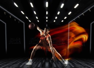 Spor salonunda antrenman yapan genç bir basketbolcu, kapalı arka planda karışık ışıkta izole edilmiş. Spor, oyun, rekabet kavramı.