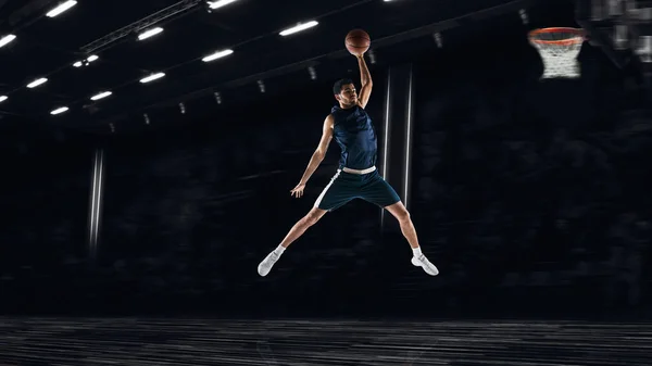 Un joven jugador de baloncesto deportista entrenando en el gimnasio, ídolos aislados en el fondo oscuro. Concepto de deporte, juego, competencia. Golpe de clavo. Collage. — Foto de Stock