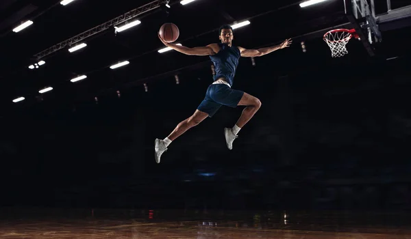 Young African sportsman, basketball player jumping high isolated on dark background. Concept of sport, game, competition. Dynamic — Stock Photo, Image