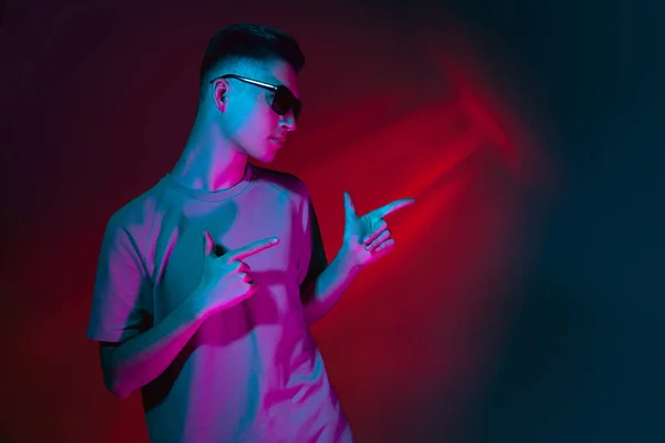 Porträt eines kaukasischen jungen Mannes mit Sonnenbrille isoliert auf dunkelrotem Studiohintergrund in neonrosa Licht. Konzept menschlicher Emotionen, Mimik. — Stockfoto