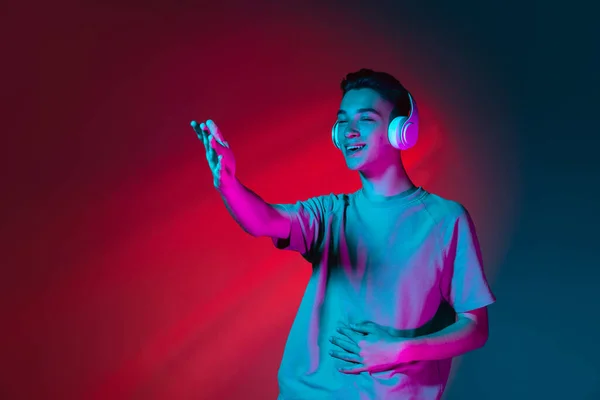 Portré kaukázusi fiatalemberről fülhallgatóban, sötét vörös stúdió háttérrel, neon rózsaszín fényben. Az emberi érzelmek fogalma, arckifejezés. — Stock Fotó