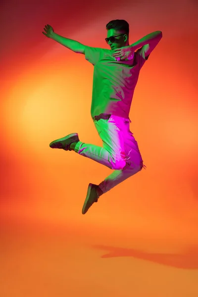 Portret van Kaukasische jongeman springend, dansend geïsoleerd op oranje studio achtergrond in neon licht. Concept van menselijke emoties, gezichtsuitdrukking. — Stockfoto