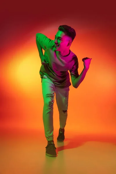 Retrato de caucasiano jovem dançando, dançando isolado em fundo estúdio laranja em luz de néon. Conceito de emoções humanas, expressão facial. — Fotografia de Stock