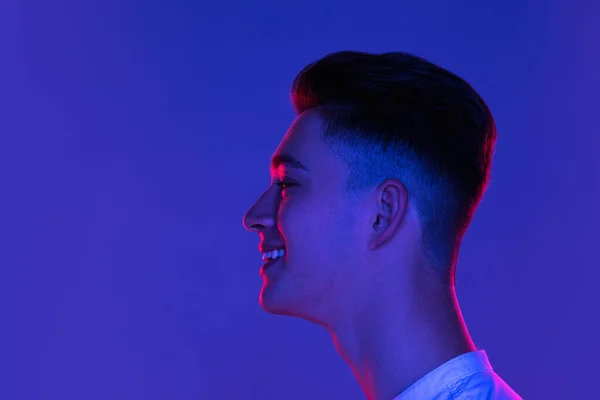Gros plan Jeune homme caucasien posant isolé sur fond bleu studio en néon rose clair. Concept d'émotions humaines, expression faciale. — Photo