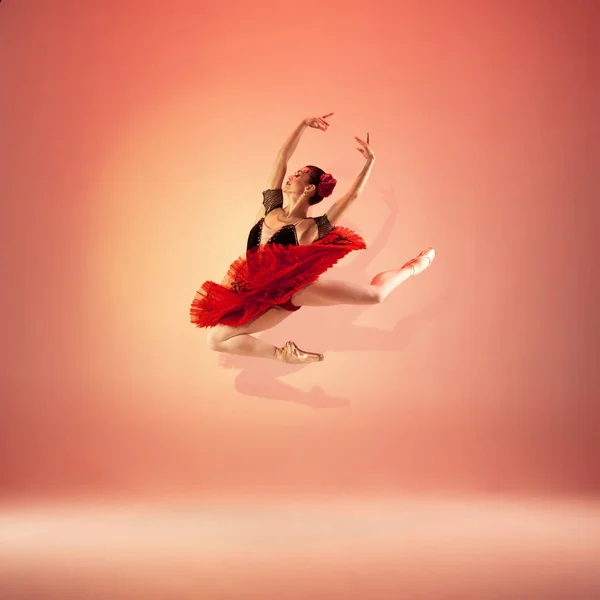 Jovem e incrivelmente bela bailarina está posando e dançando no estúdio vermelho cheio de luz. — Fotografia de Stock