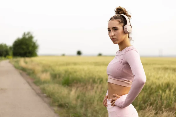 Jovem corredora, atleta está correndo na estrada em sol de verão. Bela mulher caucasiana a treinar, a ouvir música. Conceito de esporte, estilo de vida saudável, movimento, atividade. — Fotografia de Stock