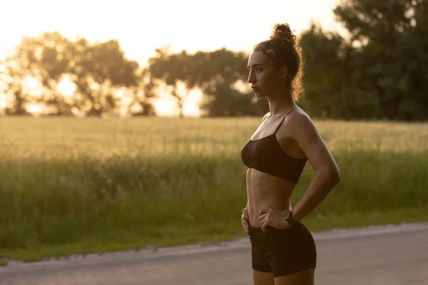 Joven corredora, atleta está trotando en la carretera bajo el sol del verano. Hermosa mujer caucásica entrenando, escuchando música. Concepto de deporte, estilo de vida saludable, movimiento, actividad. — Foto de Stock