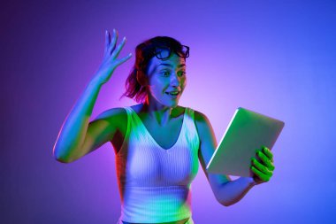 Elinde tablet var, çok heyecanlı. Siyah stüdyo arka planında neon ışıkta beyaz kadın portresi. Beyaz gömlekli güzel erkek model..