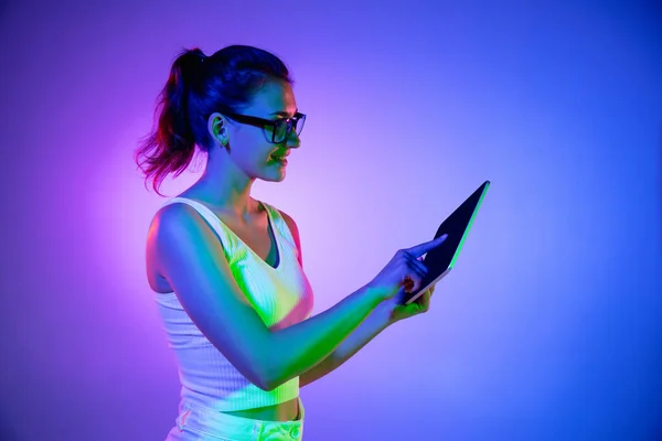 A segurar o tablet, muito excitado. Retrato de mulheres jovens caucasianas no fundo do estúdio preto em luz de néon. Modelo masculino bonito em camisa branca. — Fotografia de Stock