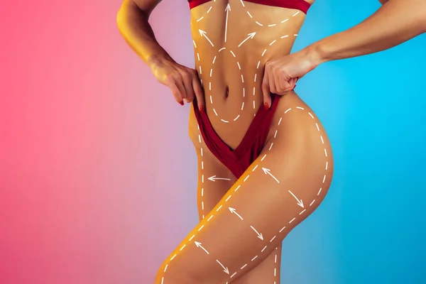 Cuerpo femenino bonito de primer plano con flechas aisladas sobre fondo azul rosado degradado. Concepto de dieta, deportes, cirugía plástica. —  Fotos de Stock