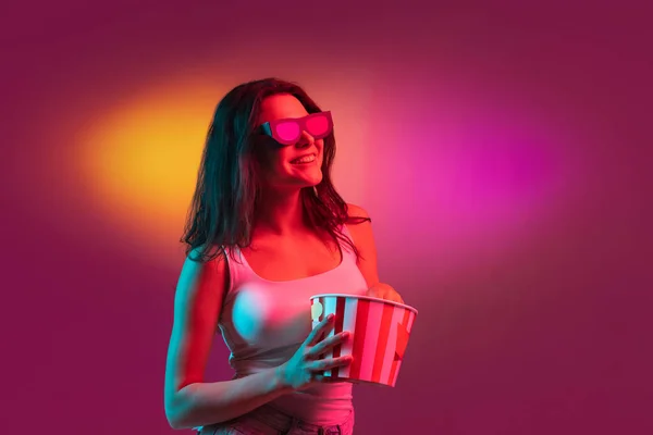 3D 안경 과 팝콘을 쓰고 있습니다. 백인 여성 사진 이 붉은 색 스튜디오 배경에 핑크 네온 빛으로 분리되어 있습니다. 아름다운 남성 모델. — 스톡 사진
