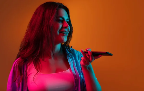 Grabando mensaje de voz. Retrato moderno para mujer sobre fondo de estudio naranja degradado en neón. — Foto de Stock